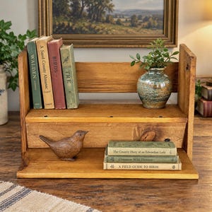 May include: A two-tiered wooden bookshelf with a natural finish, holding seven books titled Walden, A Sand County Almanac, Birds, Tre, The Country Diary of an Edwardian Lady, Common Wild Flowers, and A Field Guide to Birds, plus a ceramic vase and bird figurine.