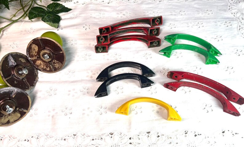 May include: Assortment of vintage cabinet knobs in various colors, including red, green, black, and yellow. The knobs are made of plastic and have a rounded, arched shape.