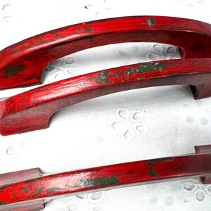 May include: Three red painted metal door handles with a distressed finish. The handles are in the shape of an arch.