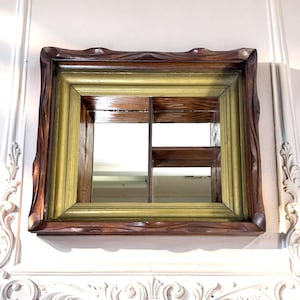 May include: A square wall-mounted display shelf featuring a dark brown wood outer frame with a wavy edge and a smooth, muted gold-toned inner frame. The interior is divided into three sections by a vertical divider and a small horizontal shelf.