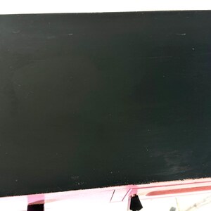 May include: A black, rectangular tabletop with a glossy finish. The table is supported by a metal frame with chrome-colored bars. The edges of the table are pink.