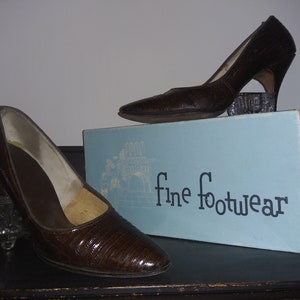 May include: Two pairs of brown leather heeled shoes with a textured pattern. The shoes are on a blue box with the text "fine footwear".