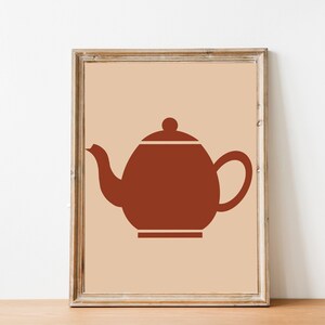 Puede incluir: Impresión enmarcada con un diseño minimalista de una tetera. La tetera es de color marrón cálido, sobre un fondo beige claro. El marco es de madera natural, añadiendo un toque rústico a la obra de arte.