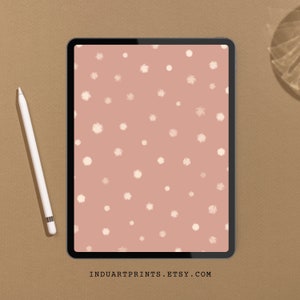 May include: A digital tablet displaying a pink background with a white polka dot pattern. The tablet is on a brown surface.