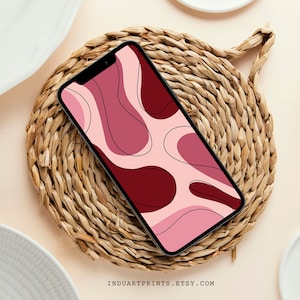 May include: A smartphone displaying a pink and burgundy abstract pattern wallpaper with black outlines. The phone is lying on a woven wicker surface.