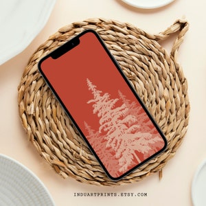 May include: A red phone wallpaper with a white silhouette of a pine forest. The phone is on a woven straw coaster.