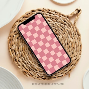 May include: A black smartphone with a pink and white checkered pattern on the screen. The phone is lying on a woven straw mat.