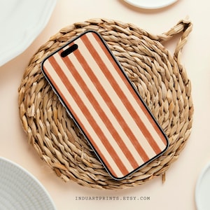 May include: A smartphone case with a vertical striped pattern in shades of orange and cream. The case is resting on a woven, circular placemat. The Etsy shop name, INDUARTPRINTS.ETSY.COM, is printed at the bottom.