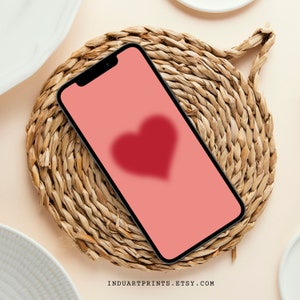 Può includere: Uno smartphone con uno schermo rosa e una forma di cuore rossa sullo schermo. Il telefono è su un tappetino di paglia intrecciato.