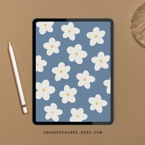 May include: A digital tablet displaying a blue background with a white daisy pattern. The tablet is on a brown surface.