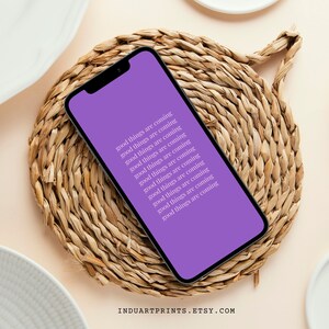 Puede incluir: Una pantalla de teléfono púrpura con el texto "good things are coming" repetido varias veces. El teléfono está sobre una estera de paja tejida.