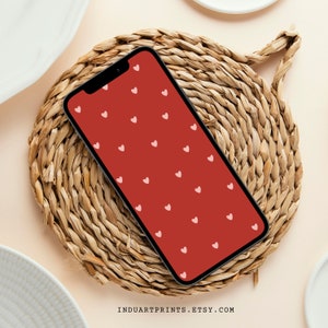 Könnte beinhalten: Eine rote Handyhülle mit einem Muster aus kleinen rosa Herzen. Die Hülle liegt auf einem geflochtenen Stroh-Untersetzer.