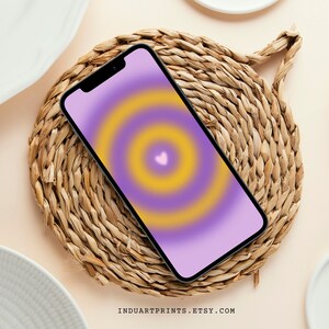 May include: A purple and yellow gradient phone wallpaper with a small pink heart in the center. The wallpaper is displayed on a smartphone.
