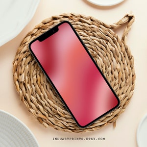 Op de afbeelding: Een zwarte smartphone met een rood verloopscherm ligt op een geweven strooien onderzetter.