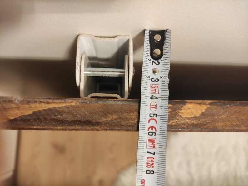 K&ouml;nnte beinhalten: Nahaufnahme einer Metallhalterung mit einem Ma&szlig;band daneben. Die Halterung ist hellgrau und rechteckig. Das Ma&szlig;band zeigt ein Ma&szlig; von ca. 5 cm an.