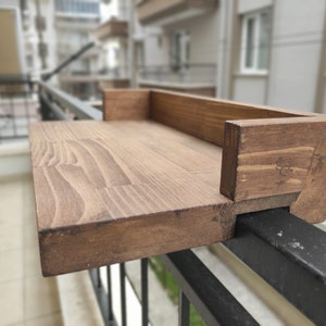 May include: A wooden shelf attached to a black metal railing. The shelf is stained a dark brown color and has a simple design.
