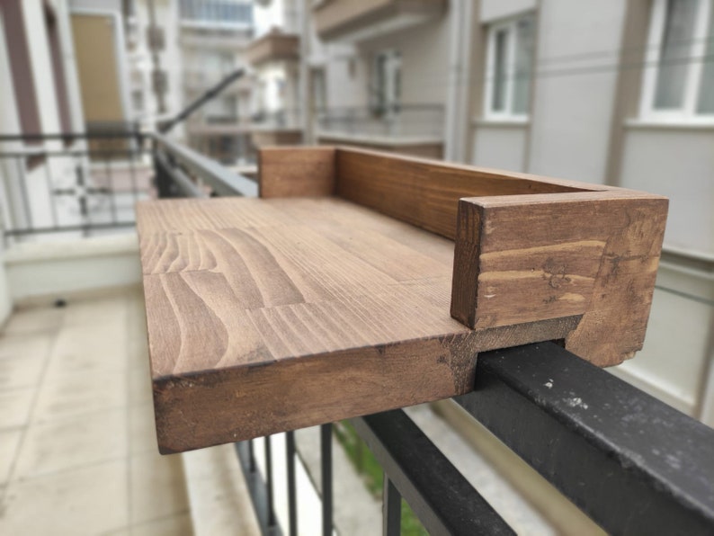 May include: A wooden shelf attached to a black metal railing. The shelf is stained a dark brown color and has a simple design.