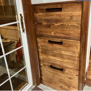 May include: Three wooden drawers with black metal handles. The drawers are stacked vertically and are made of a light brown wood with a natural finish.