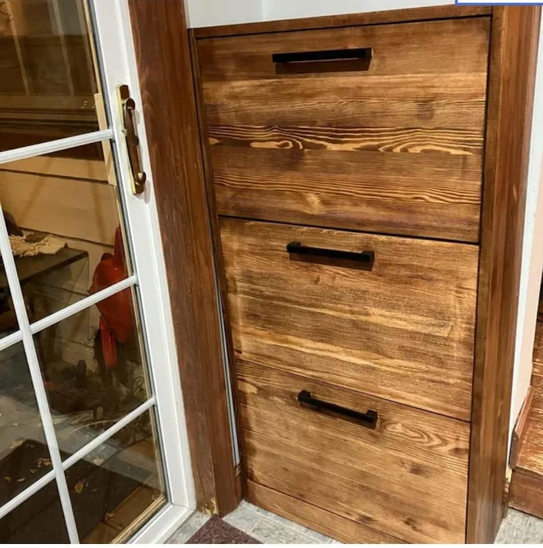 May include: Three wooden drawers with black metal handles. The drawers are stacked vertically and are made of a light brown wood with a natural finish.