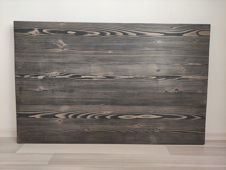 K&ouml;nnte beinhalten: Eine rechteckige Holzplatte mit dunkelgrauer Beize, die die nat&uuml;rliche Holzmaserung und die Knoten zeigt. Die Platte besteht aus mehreren horizontalen Brettern und erzeugt eine rustikale und strukturierte Oberfl&auml;che. Sie ist ca. 91 cm breit und 61 cm hoch.