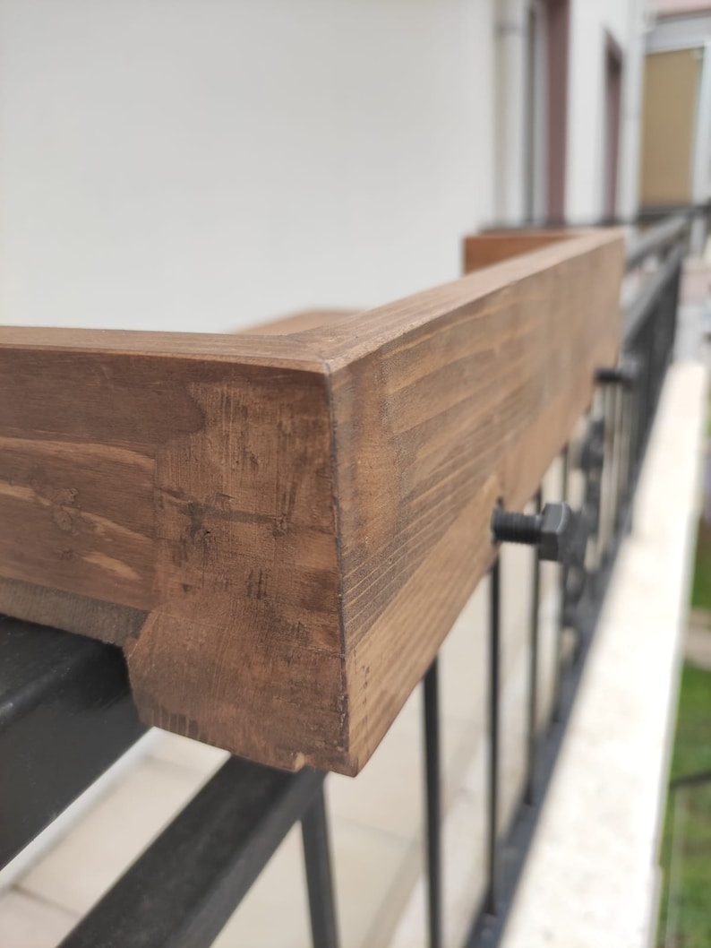 May include: Close-up of a wooden balcony railing with a dark brown stain. The railing is attached to a black metal railing with screws.