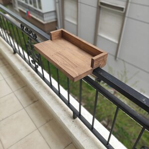 May include: A wooden shelf attached to a black metal railing. The shelf is stained a dark brown color and has a simple design.