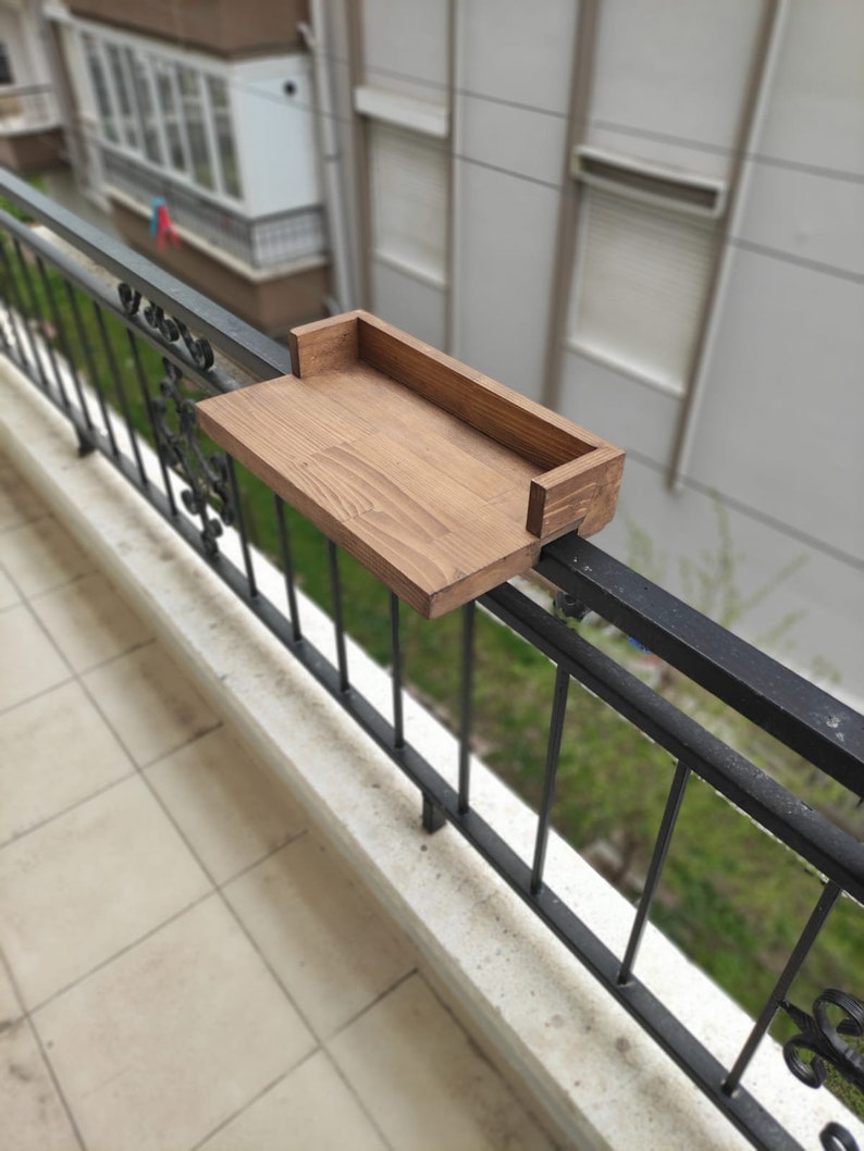 May include: A wooden shelf attached to a black metal railing. The shelf is stained a dark brown color and has a simple design.