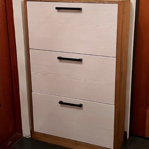 May include: A white three-drawer shoe cabinet with black handles and a wood frame.