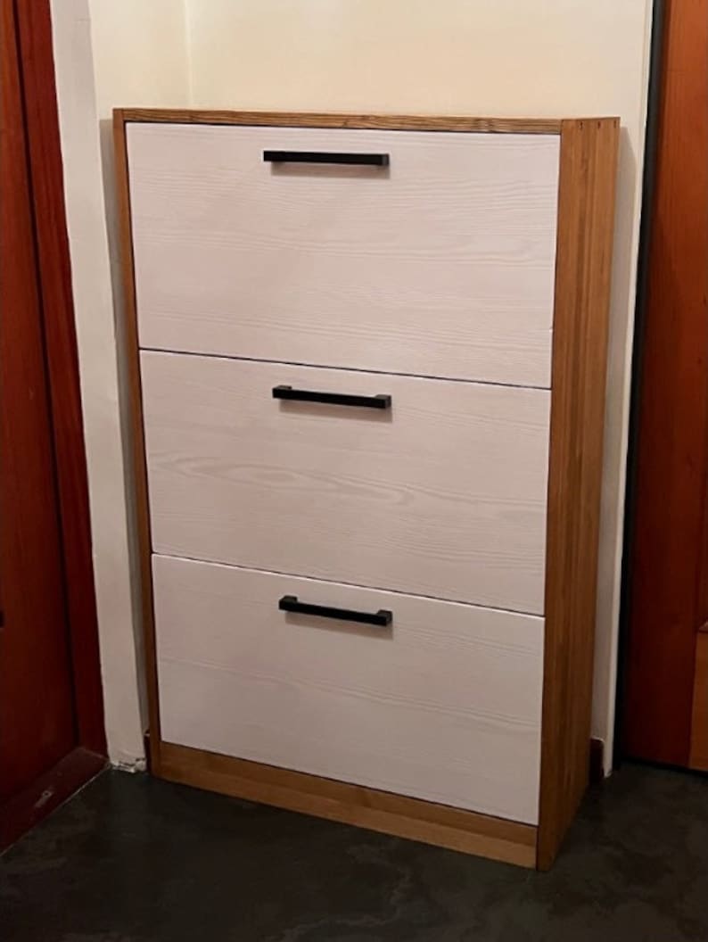May include: A white three-drawer shoe cabinet with black handles and a wood frame.