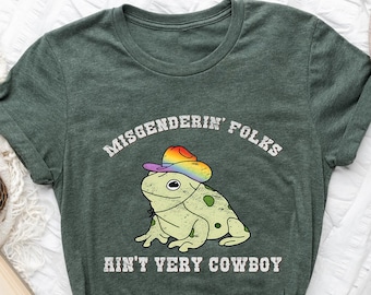 May include: A green t-shirt with a frog wearing a rainbow cowboy hat. The text on the shirt reads "Misgenderin' Folks Ain't Very Cowboy".