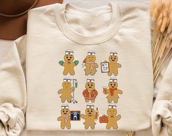 May include: Cream-colored sweatshirt featuring a repeating pattern of gingerbread people dressed as nurses. Each gingerbread figure has a white nurse's cap and is holding various medical items. The design is a fun, festive take on healthcare.