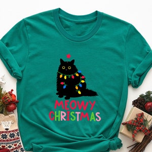 May include: A teal green t-shirt with a black cat wearing Christmas lights and the text "MEOWY CHRISTMAS" in rainbow colors.
