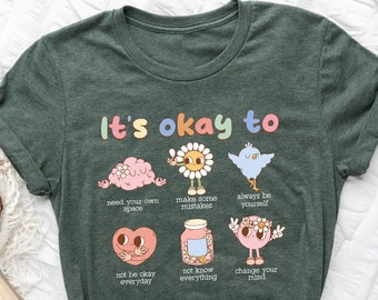 May include: Green t-shirt with the text "It's okay to" and illustrations of various characters with positive affirmations. The affirmations include "need your own space", "make some mistakes", "always be yourself", "not be okay everyday", "not know everything", and "change your mind".
