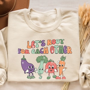 May include: A beige sweatshirt with a graphic of four cartoon vegetables and the text "Let's Root For Each Other".