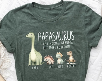 Può includere: T-shirt verde scuro con la scritta "PAPASARUS like a normal grandpa but more roarsome" e illustrazioni di dinosauri. I nomi "Papa", "Jane", "Alex" e "Robert" sono sotto. La maglietta è piegata su una superficie bianca.