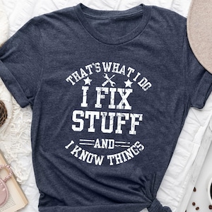 May include: A navy blue t-shirt with a white distressed graphic that reads "That's what I do I fix stuff -and- I know things".