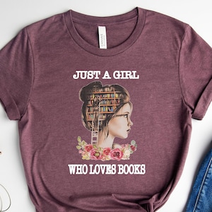 Pu&ograve; includere: Una t-shirt color marrone heather con una grafica di una donna con una libreria come testa. Il testo "Just a girl who loves books" &egrave; stampato sulla t-shirt.