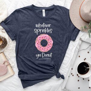 May include: A heather navy blue t-shirt with a pink donut graphic and the text "whatever sprinkles ya donut".