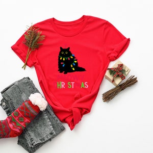 May include: Red t-shirt with a black cat wearing colorful Christmas lights and the text "MEOWY CHRISTMAS".