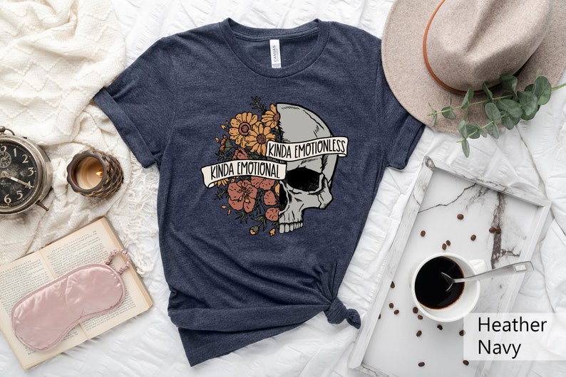 Pu&ograve; includere: Una t-shirt blu navy con un motivo a forma di teschio. Met&agrave; del teschio &egrave; ricoperta di fiori e il testo "Kinda Emotional", mentre l'altra met&agrave; &egrave; liscia con il testo "Kinda Emotionless".