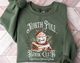 May include: Green sweatshirt with a graphic design featuring a mug of hot cocoa, gingerbread man, and the words "North Pole Book Club." The design includes the text "Read" on the mug and "Hot Cocoa Served Daily."