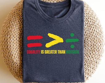 Può includere: Una maglietta blu scuro con un design grafico di un segno uguale, un segno maggiore di e un segno di divisione. Il grafico è in rosso, giallo e verde. Il testo "L'uguaglianza è maggiore della divisione" è stampato sotto il grafico.