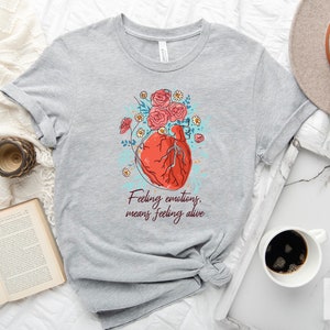 May include: Grey t-shirt with a graphic of a red heart with flowers and the text "Feeling emotions, means feeling alive".