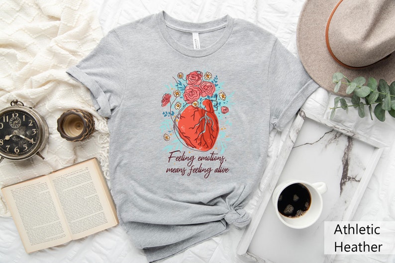 May include: Grey t-shirt with a graphic of a red heart with flowers and the text "Feeling emotions, means feeling alive".