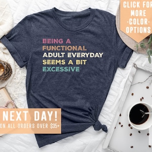 May include: A navy blue t-shirt with the text "Being a Functional Adult Everyday Seems a Bit Excessive" in colorful retro-style lettering.
