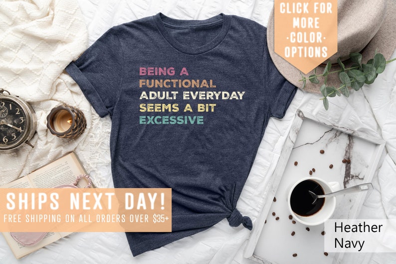 May include: A navy blue t-shirt with the text "Being a Functional Adult Everyday Seems a Bit Excessive" in colorful retro-style lettering.