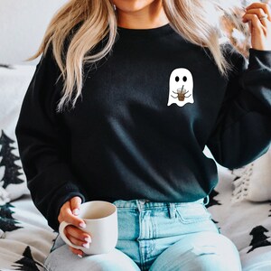 Puede incluir: Sudadera negra con un gr&aacute;fico de fantasma blanco sosteniendo una taza de caf&eacute;. El fantasma tiene una expresi&oacute;n amigable. La sudadera es de estilo casual, adecuada para el uso diario. El dise&ntilde;o es simple y juguet&oacute;n, perfecto para Halloween o los amantes del caf&eacute;.
