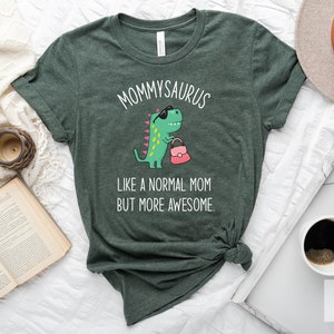 May include: Heather forest green t-shirt with the text "MOMMYSAURUS" above a cartoon dinosaur wearing sunglasses and carrying a pink purse. The text "LIKE A NORMAL MOM BUT MORE AWESOME" is below the dinosaur.