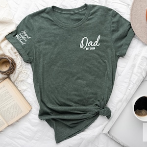 May include: A dark green t-shirt with the text "Dad Est 2024" on the front and the names "Abigail, Sophia, Michael" on the sleeve.