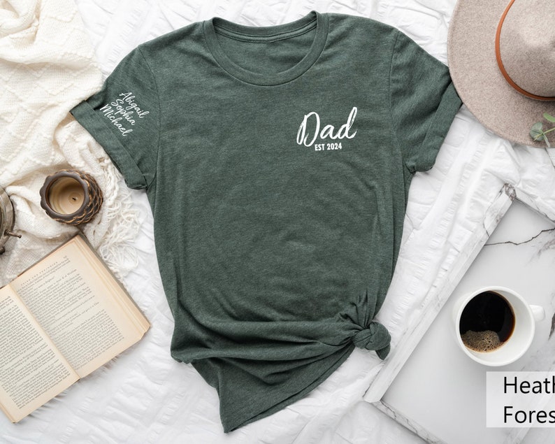 May include: A dark green t-shirt with the text "Dad Est 2024" on the front and the names "Abigail, Sophia, Michael" on the sleeve.